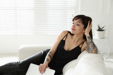 Photo of Beautiful woman with tattoos on arms resting in living room