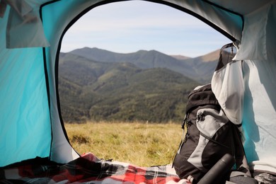 Photo of Camping tent with backpack and thermos in mountains on sunny day, view from inside