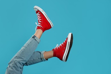 Woman in stylish gumshoes on light blue background, closeup. Space for text