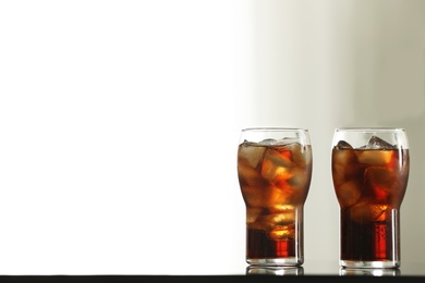 Photo of Glasses with cola and ice cubes on table against blurred background. Space for text