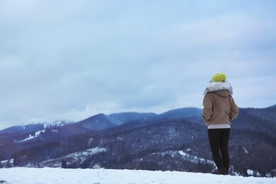 Photo of Woman in warm clothes enjoying mountain landscape, space for text. Winter vacation