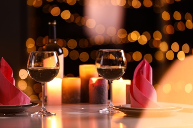 Photo of Romantic table setting with glasses of wine and burning candles against blurred background