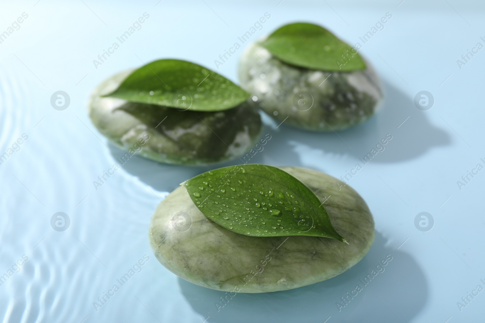 Photo of Spa stones and green leaves on light blue background, closeup