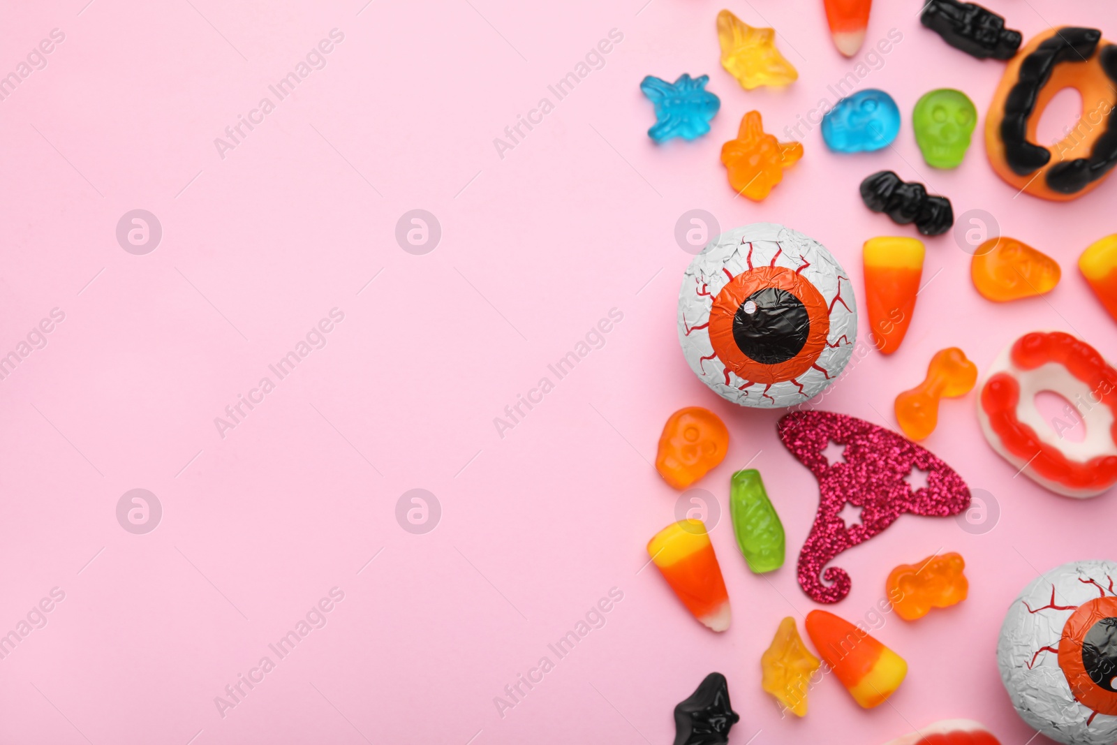 Photo of Tasty colorful jelly candies and Halloween decorations on pink background, flat lay. Space for text