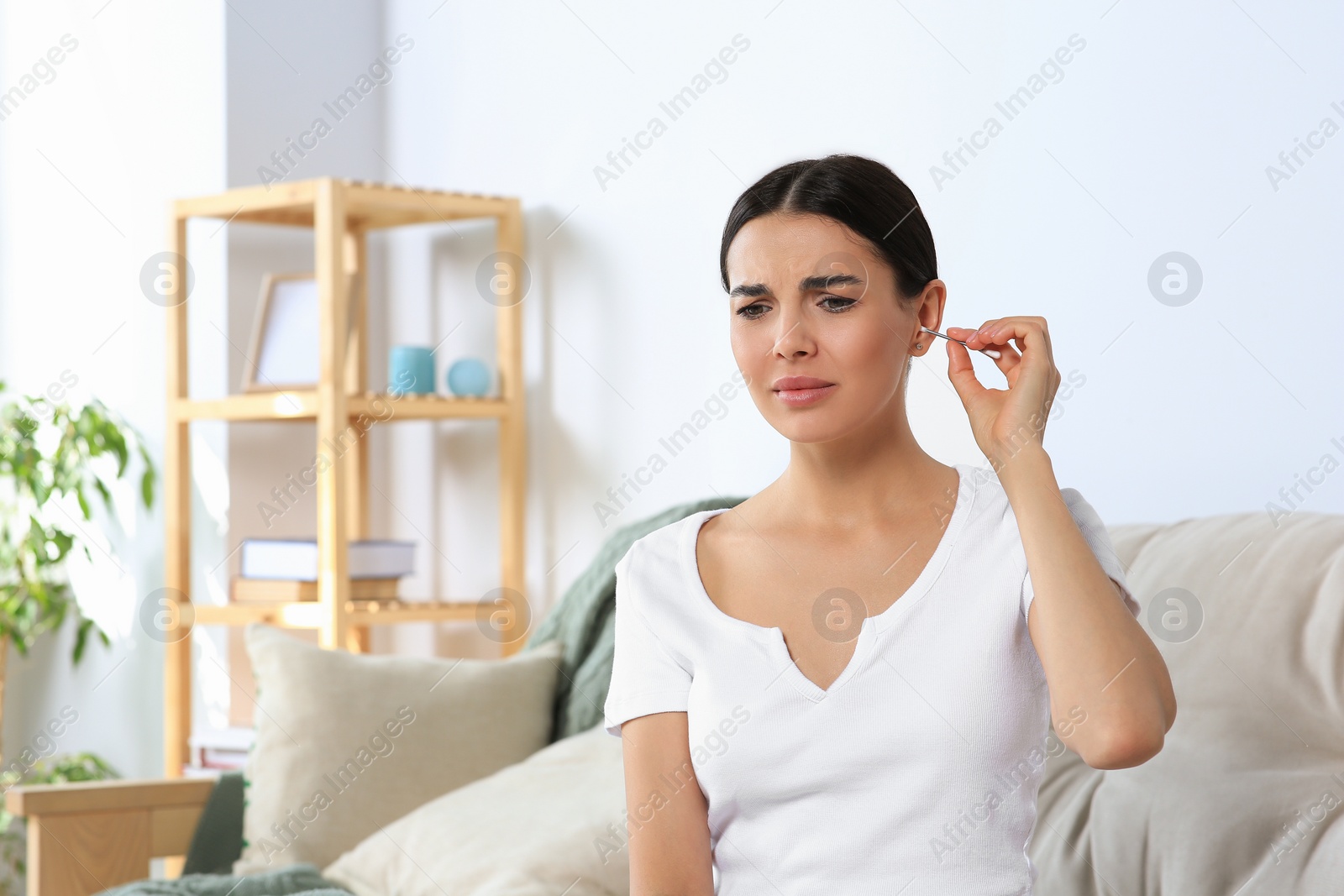 Photo of Young woman cleaning ear with cotton swab at home