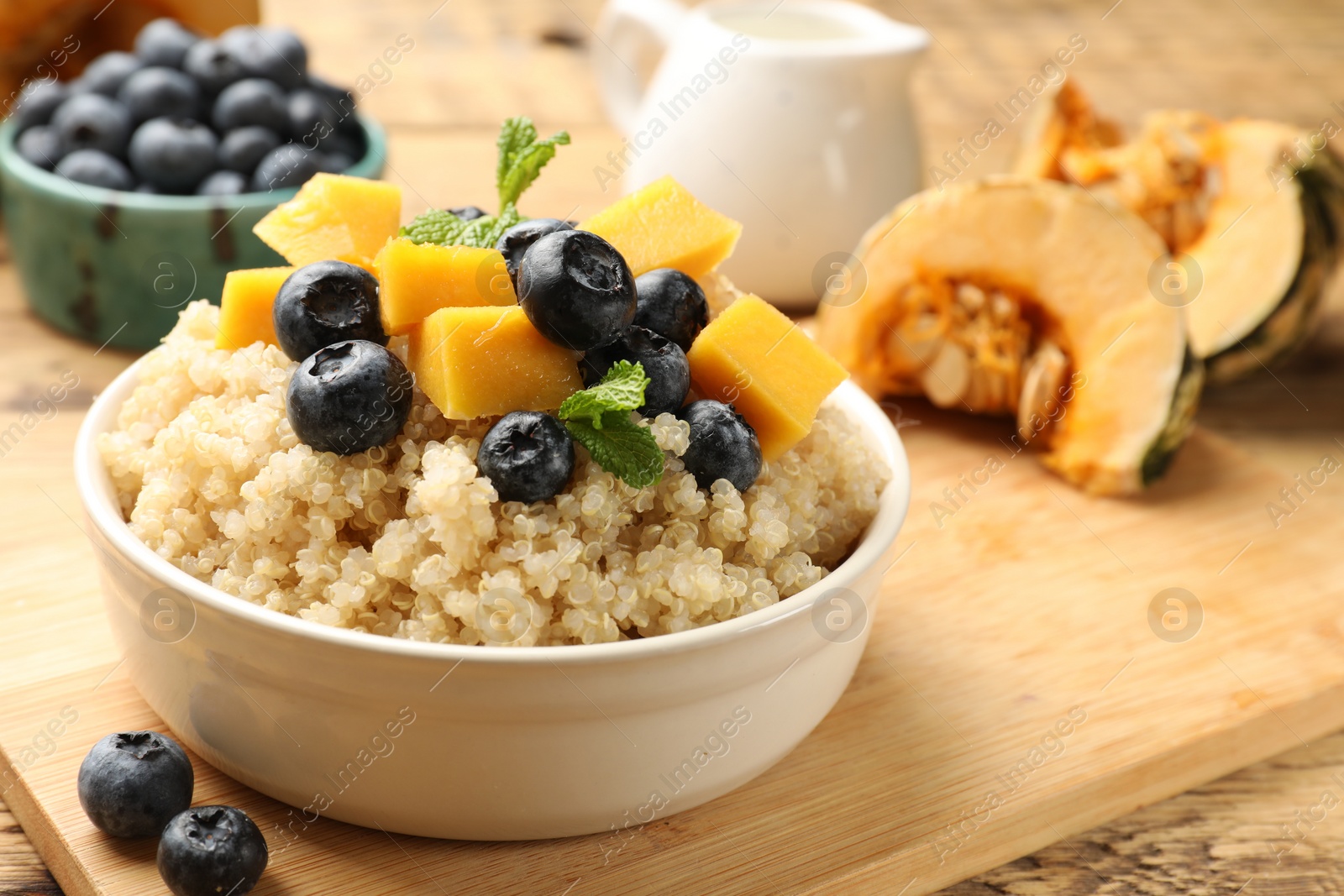 Photo of Tasty quinoa porridge with blueberries, pumpkin and mint in bowl on wooden table, closeup