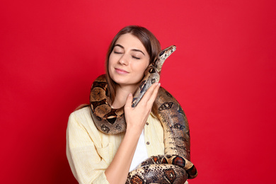 Photo of Young woman with boa constrictor on red background. Exotic pet