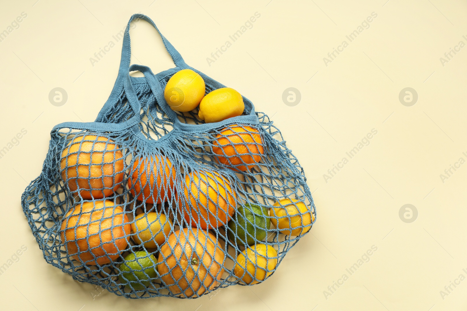 Photo of String bag with different fruits on beige background, top view. Space for text