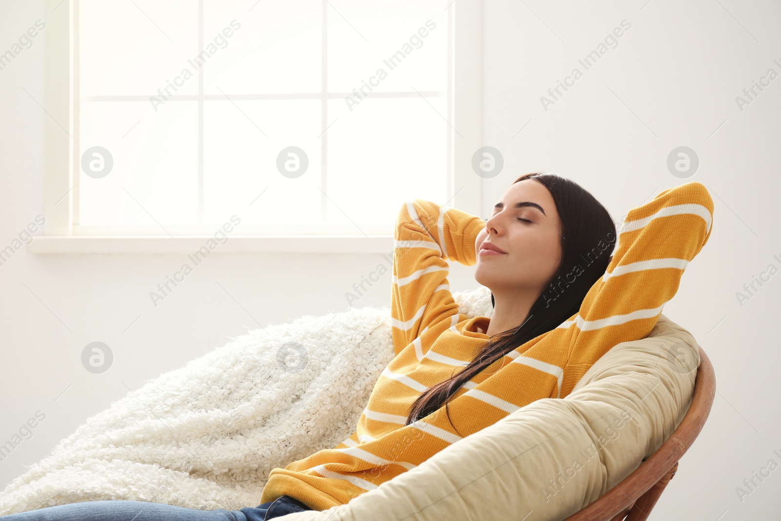 Photo of Young woman relaxing in papasan chair near window at home