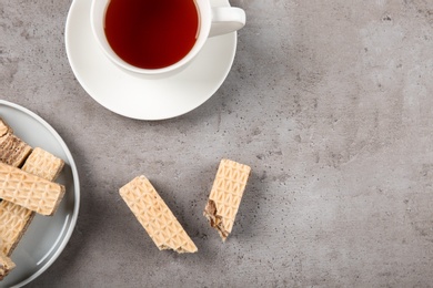 Photo of Plate of delicious wafers with cup of tea on grey stone background, top view. Space for text