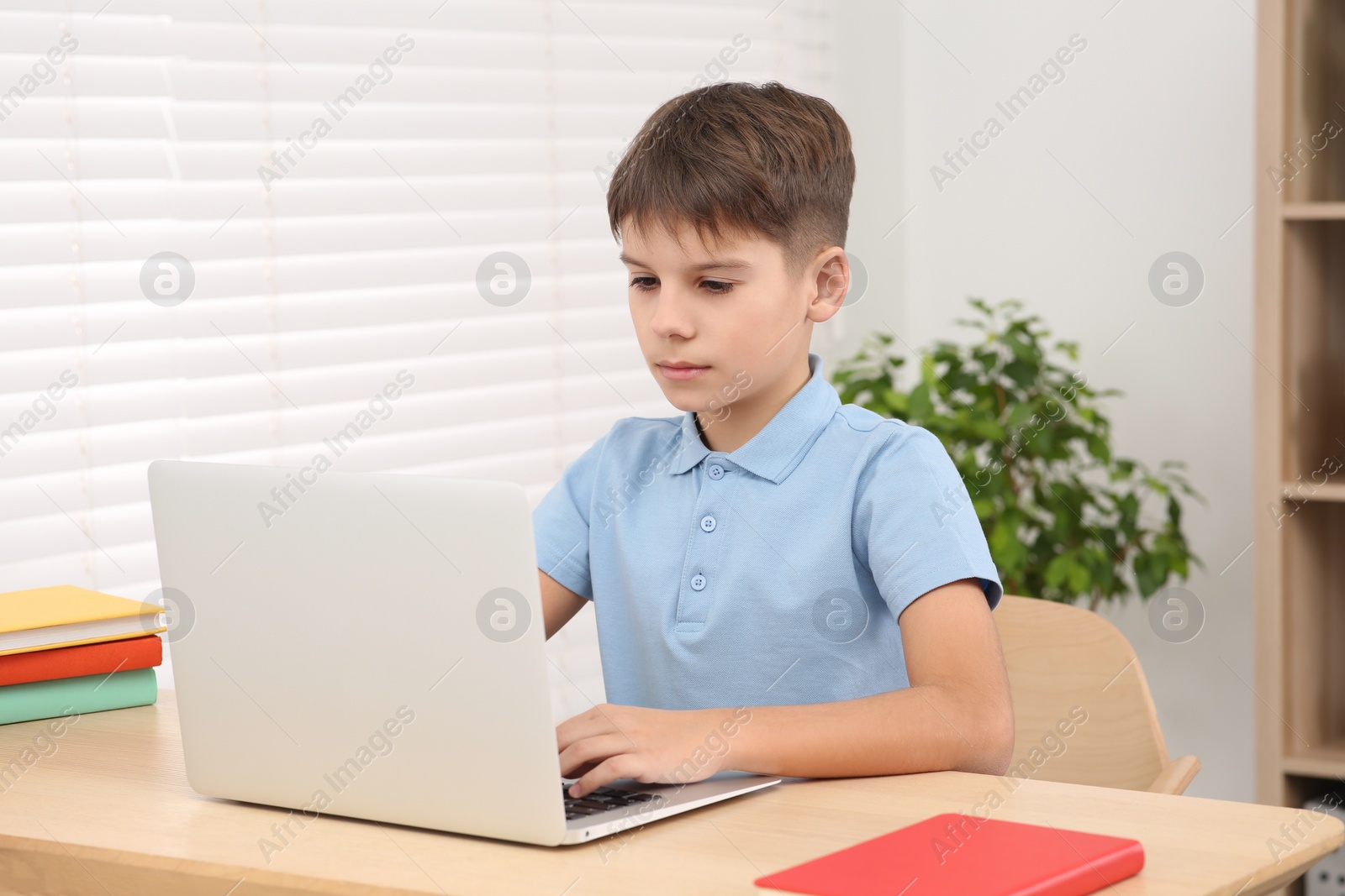 Photo of Boy using laptop at desk in room. Home workplace