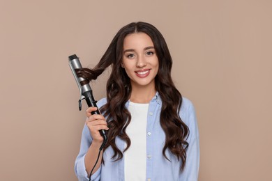 Photo of Happy woman using curling hair iron on beige background