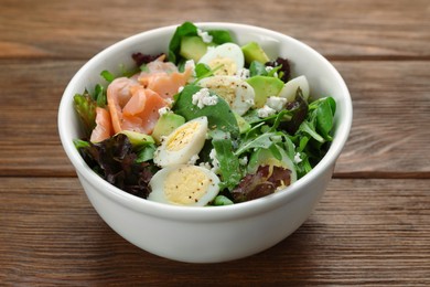 Delicious salad with boiled eggs, salmon and cheese in bowl on wooden table, closeup