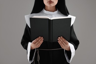 Nun reading Bible on grey background, closeup