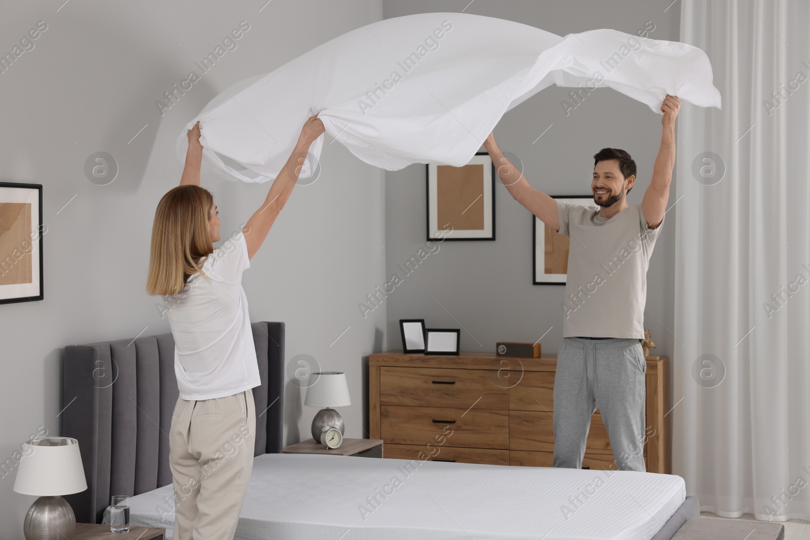 Photo of Couple changing bed linens in room. Domestic chores