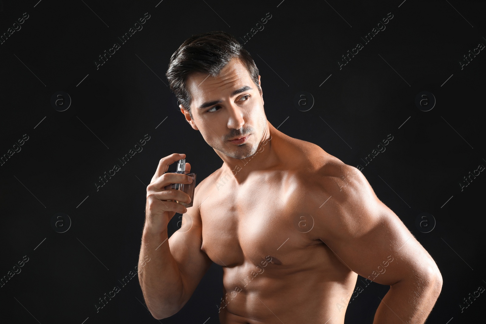 Photo of Handsome young man using perfume on black background