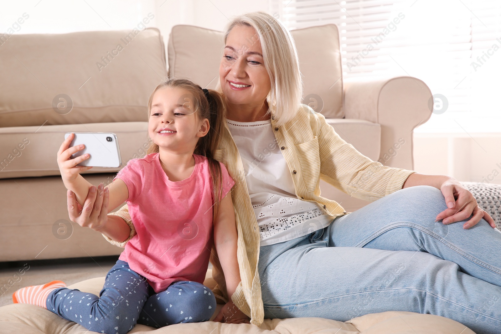 Photo of Mature woman and her little granddaughter taking selfie together at home