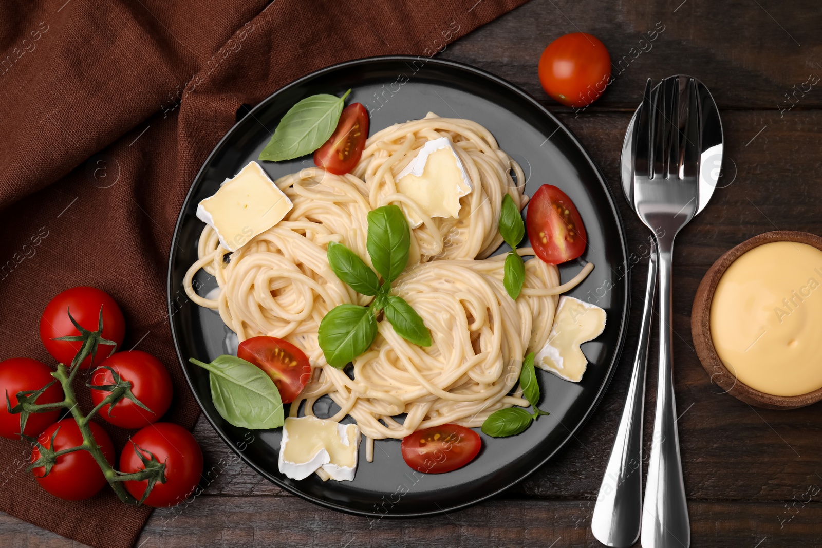 Photo of Delicious pasta with brie cheese, tomatoes and basil served on wooden table, flat lay