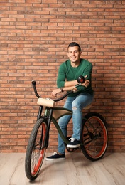 Portrait of handsome young man with bicycle near brick wall