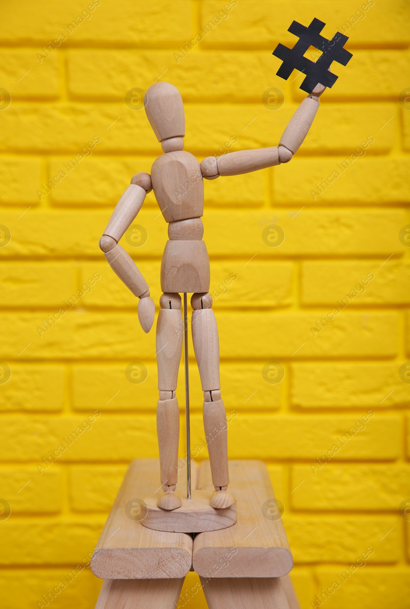 Photo of Wooden mannequin holding paper hashtag symbol near yellow brick wall