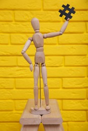 Photo of Wooden mannequin holding paper hashtag symbol near yellow brick wall