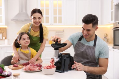 Photo of Happy family making dinner together in kitchen, father using modern meat grinder