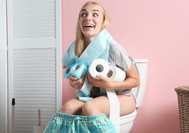 Woman with paper rolls sitting on toilet bowl in bathroom