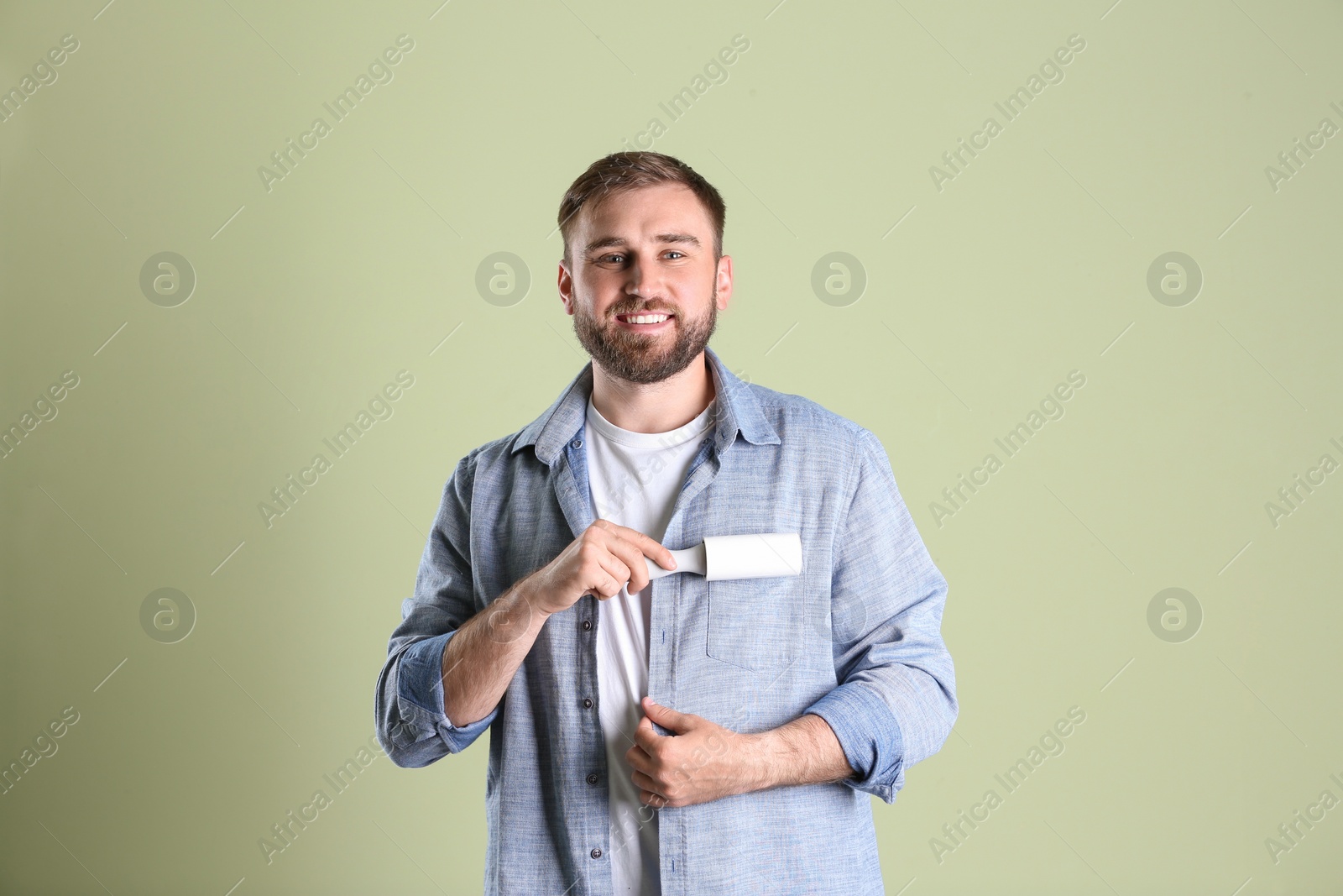 Photo of Young man cleaning clothes with lint roller on light background