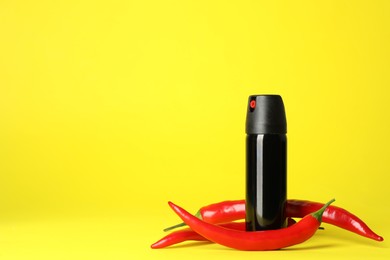 Photo of Bottle of gas pepper spray and fresh chili peppers on yellow background. Space for text