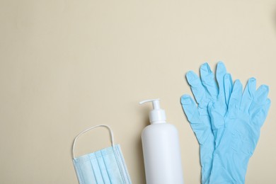 Photo of Medical gloves, mask and hand sanitizer on beige background, flat lay. Space for text