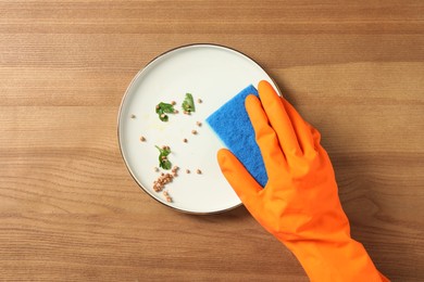 Woman washing dirty plate at wooden table, top view