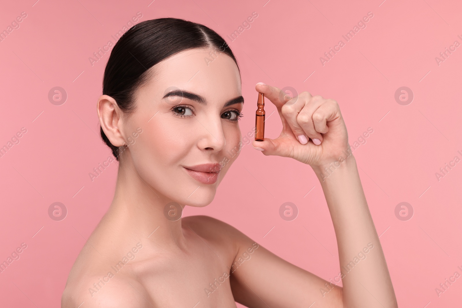 Photo of Beautiful young woman holding skincare ampoule on pink background