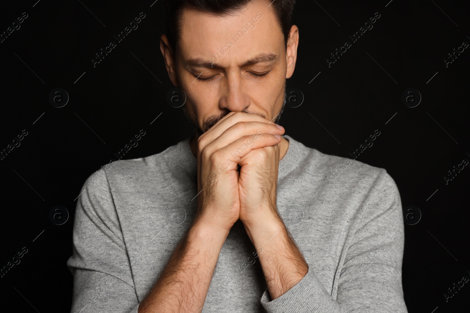 Photo of Man with clasped hands praying on black background