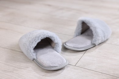 Photo of Grey soft slippers on light wooden floor at home, closeup
