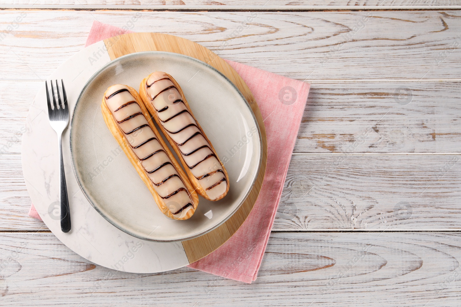 Photo of Tasty glazed eclairs served on wooden rustic table, top view. Space for text