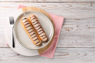 Photo of Tasty glazed eclairs served on wooden rustic table, top view. Space for text