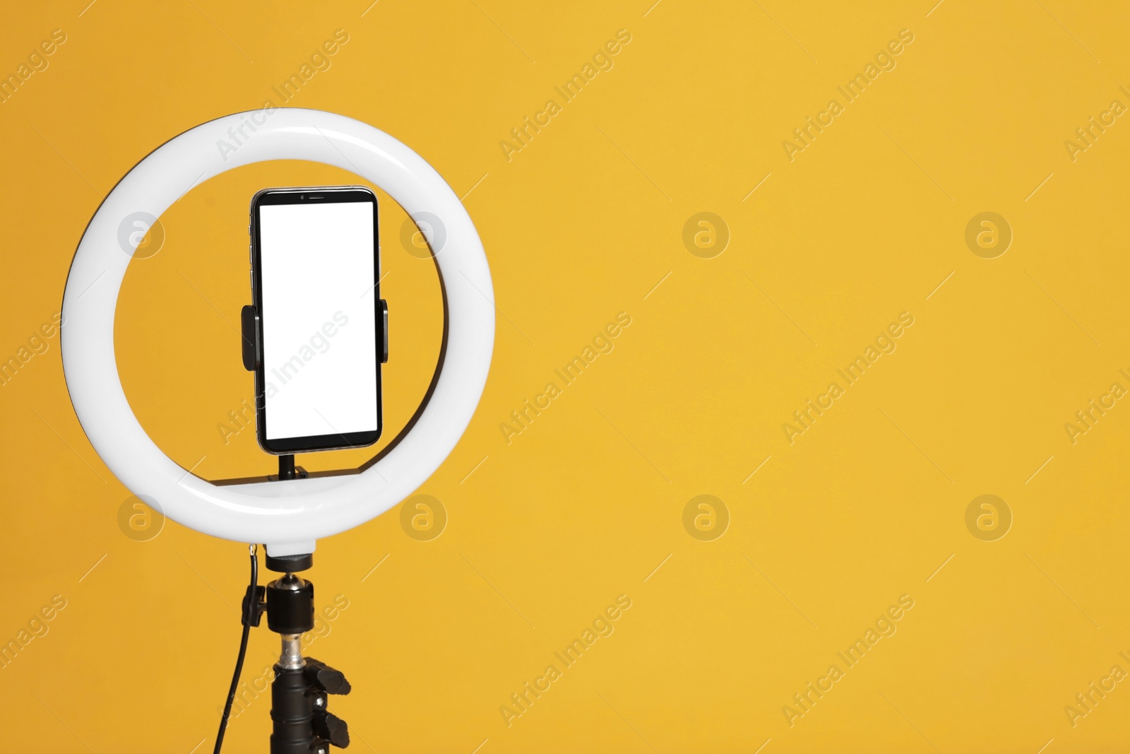 Photo of Modern tripod with ring light and smartphone on yellow background. Space for text