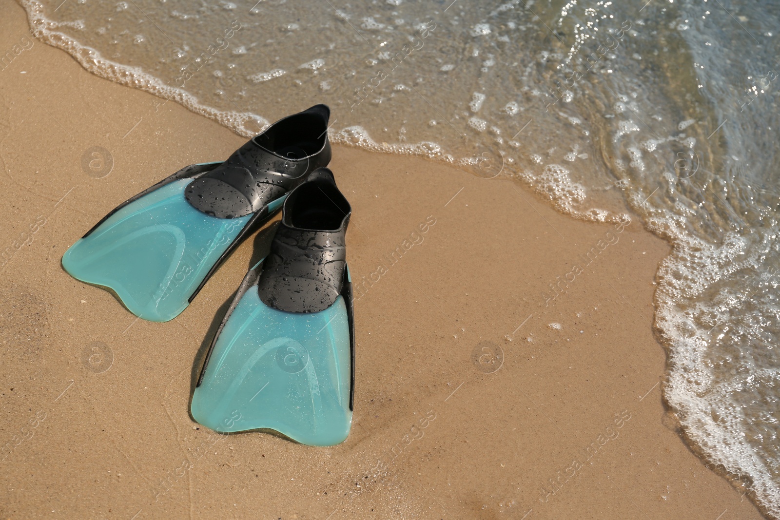 Photo of Pair of turquoise flippers on sand near sea. Space for text