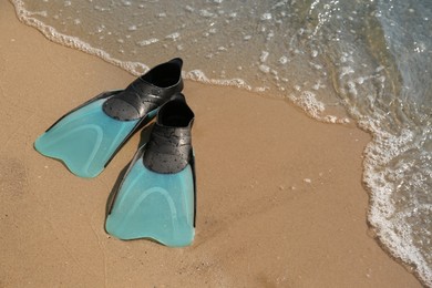 Pair of turquoise flippers on sand near sea. Space for text