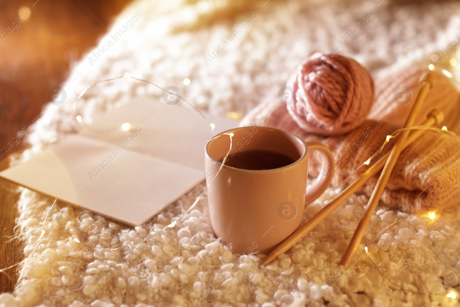 Photo of Composition with cup of hot beverage, knitting yarn and book on fuzzy rug. Winter evening