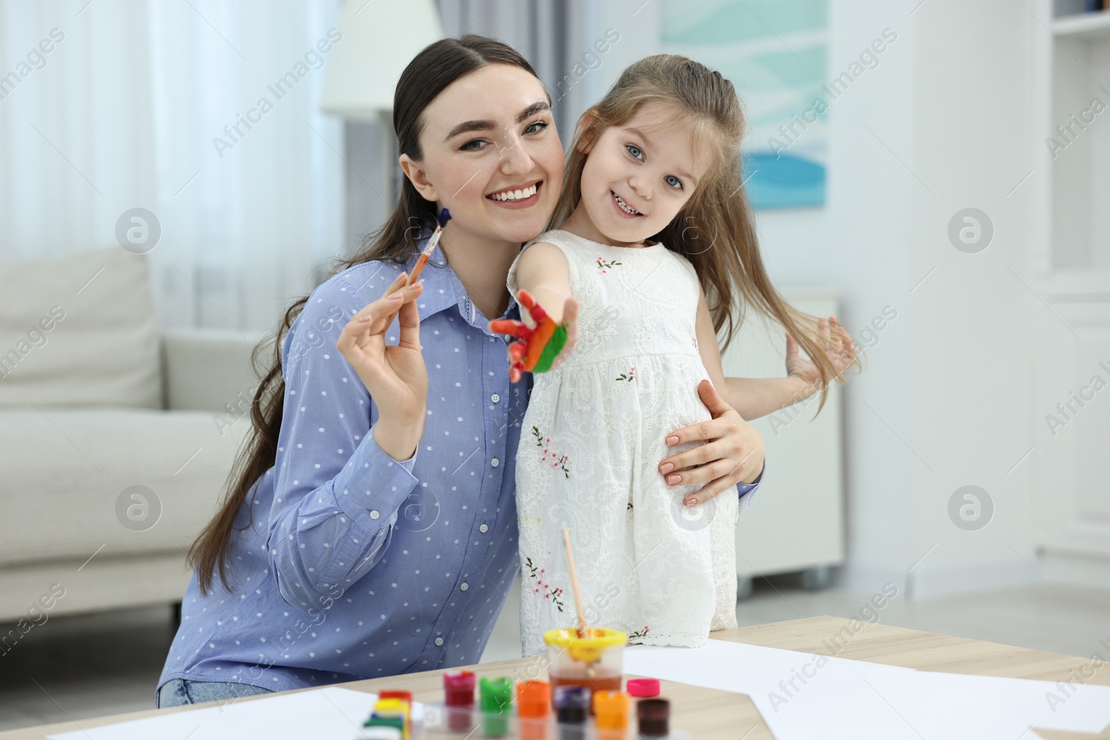 Photo of Mother and her little daughter painting with palms at home