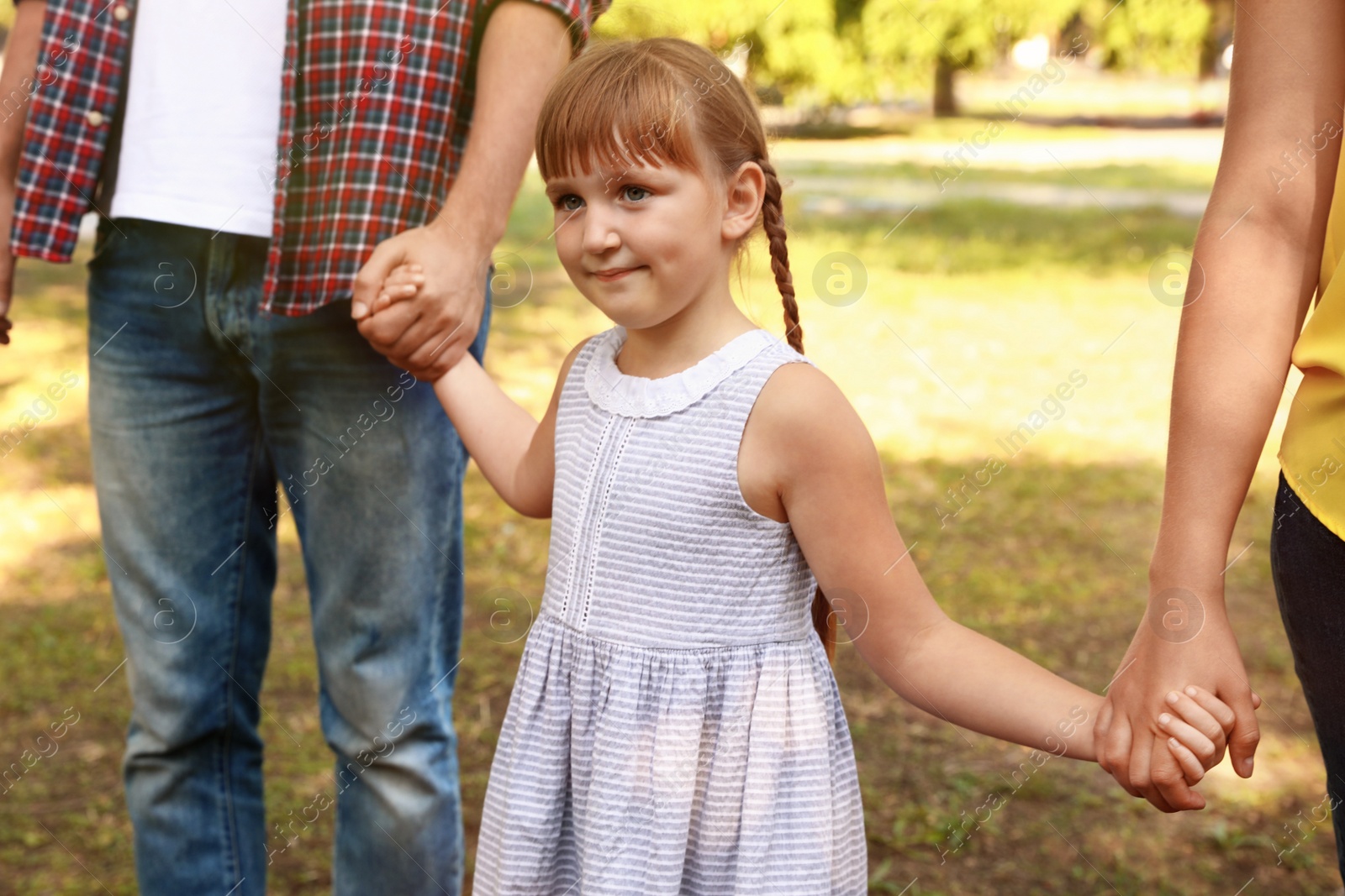 Photo of Little girl and her parents holding hands outdoors. Family weekend