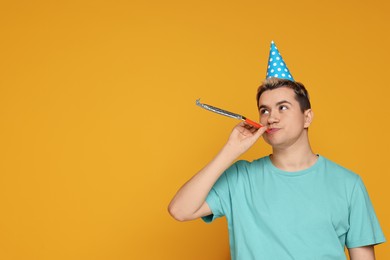 Young man with party hat and blower on orange background, space for text