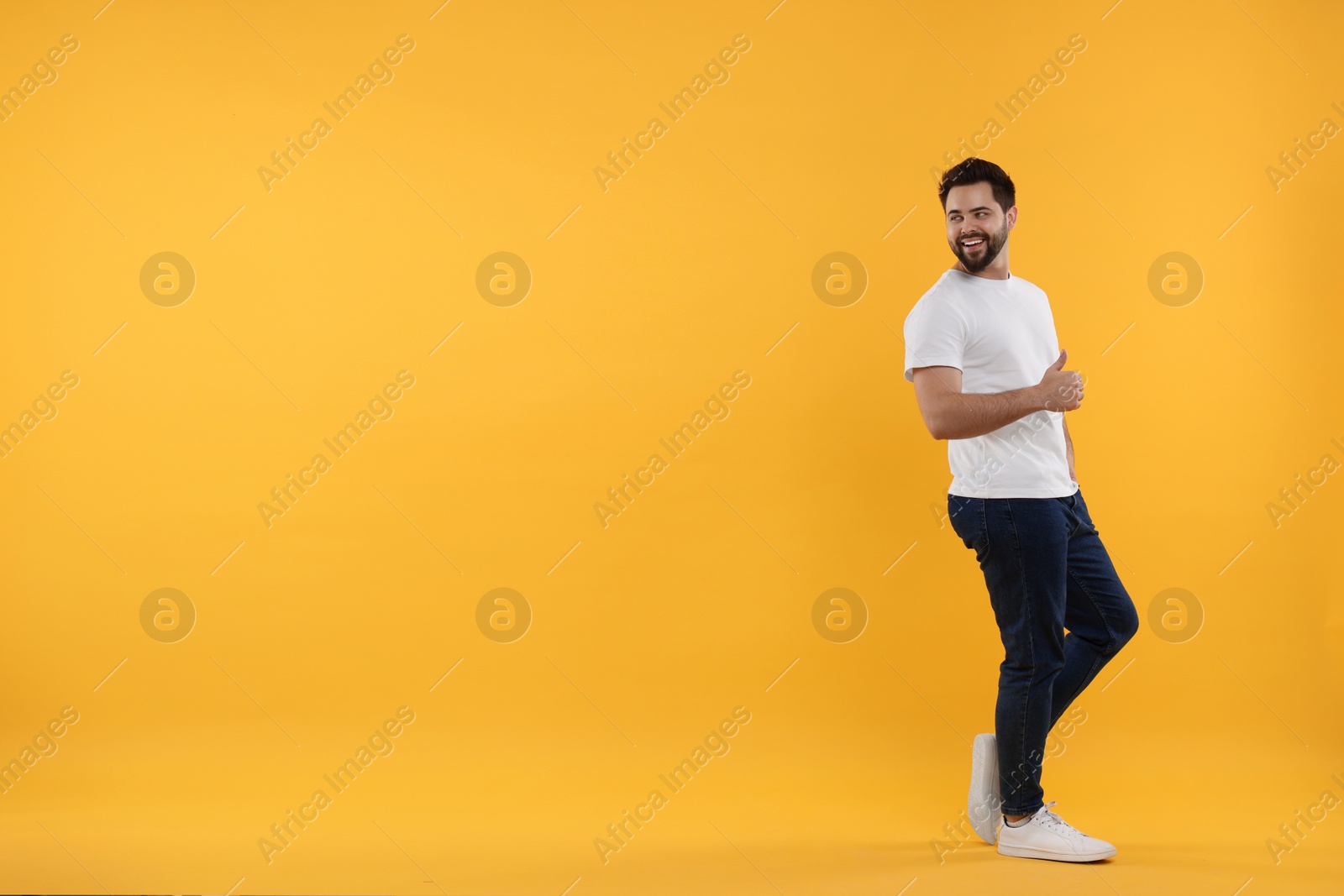 Photo of Happy young man showing thumbs up on yellow background, space for text