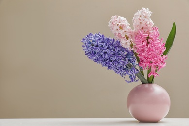 Photo of Beautiful hyacinths in vase on table against color background, space for text. Spring flowers