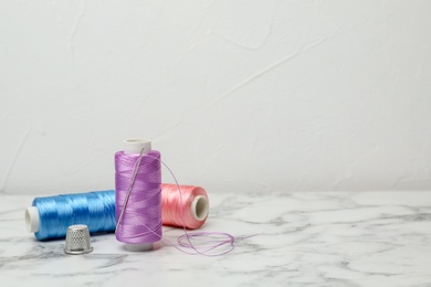 Photo of Color sewing threads, needle and thimble on table