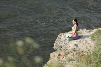 Young woman meditating on cliff near river. Space for text