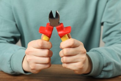 Photo of Woman with diagonal pliers at wooden table, closeup