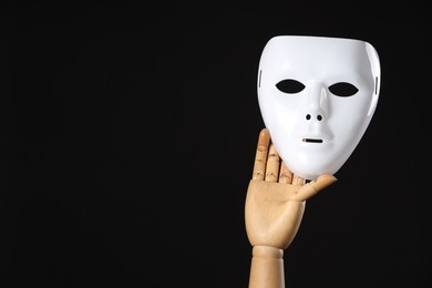 Photo of Wooden mannequin hand holding plastic mask on black background, space for text. Theatrical performance