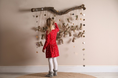 Photo of Little girl taking gift from New Year advent calendar indoors